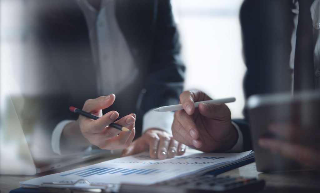 ERP & Systems Transformation Category - Closeup of hands holding pens as business team discusses and analyzes financial report