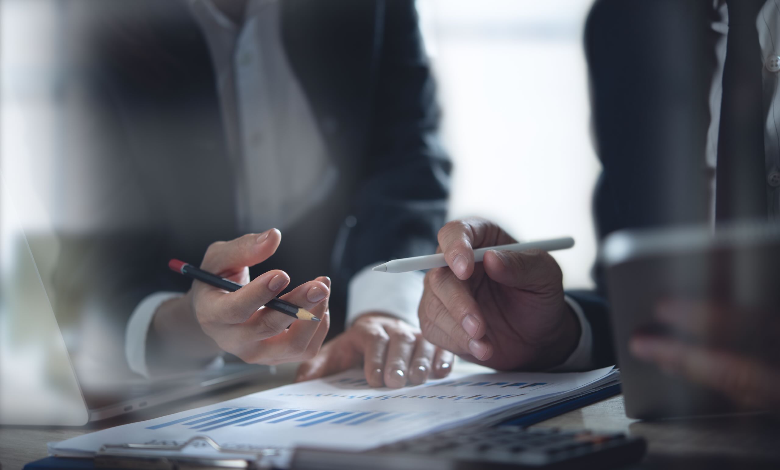 ERP & Systems Transformation Category - Closeup of hands holding pens as business team discusses and analyzes financial report